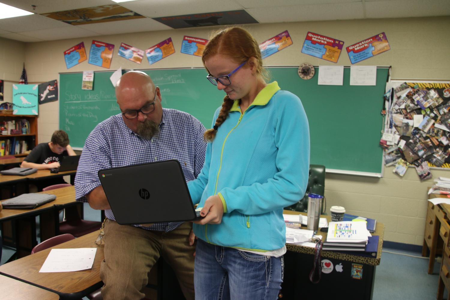 Mr. Barney, newspaper adviser, gives Hayleigh Noble advice on her cross-country article. 