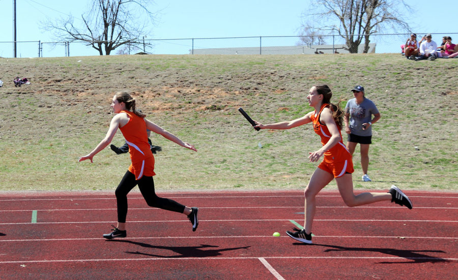 Junior Madison Rauh hands the baton to junior Hopelin Hood in their mile relay. 